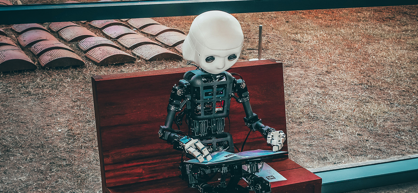 a robot sitting on a bench using a tablet computer.